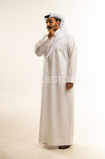 حل المشكلات واتخاذ القرارات، التطلع والتخطيط للمستقبل، بورتريه لرجل عربي خليجي قطري يرتدي الغترة والثوب التقليدييضع يده على ذقنه بإيماءات التفكير وشرود الذهن، مفهوم الاستماع والتركيز، صورة الجسم بالطول الكامل، خلفية بيضاء
