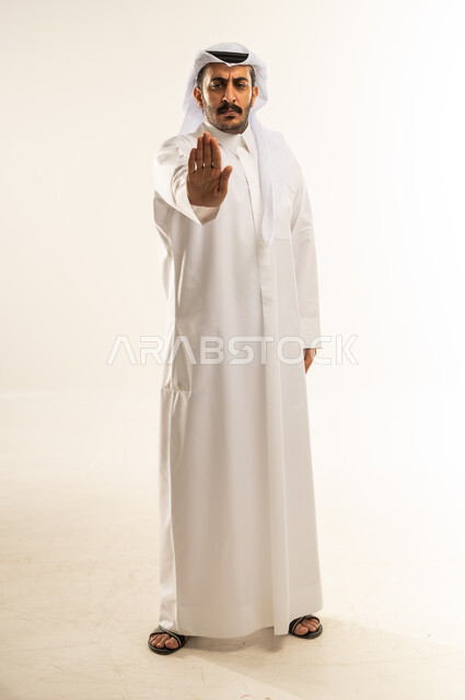 التحذير من فعل شيء ما، طلب التوقف وعدم الاقتراب, مفهوم الرفض والامتناع والانزعاج, بورتريه لرجل عربي خليجي قطري يرتدي الثوب والغترة يمد كفه نحو الأمام بإيماءات النهي عن فعل امر ما, الطول الكامل للجسم، خلفية بيضاء
