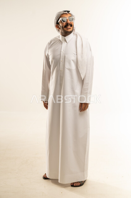 Concern about appearance, expressions of self-confidence, concept of masculinity and elegance, portrait of a Qatari Gulf Arab man wearing traditional thobe and ghutra, wearing sunglasses, looking somewhere with gestures of happiness and pleasure, full-length body image, white background