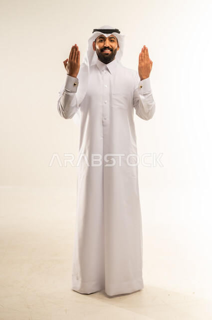عرض ظاهرة الكف، النظر الى الكاميرا بايماءات السعادة والسرور، بورتريه لرجل عربي خليجي قطري مبتسم يرتدي الثوب التقليدي والشماغ يرفع كفيه مفتوحة للاعلى، مفهوم الاناقة والاهتمام بالمظهر الخارجي، الجسم بالطول الكامل، خلفية بيضاء