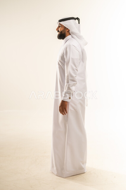 االنظر الى مكان ما بايماءات الثقة بالنفس، لاهتمام بالمظهر الخارجي, مفهوم الأناقة والرجولة, بورتريه من الجانب لرجل عربي خليجي قطري يرتدي الثوب التقليدي والغترة يقف باستقامة واعتدال, الجسم بالطول الكامل, خلفية بيضاء