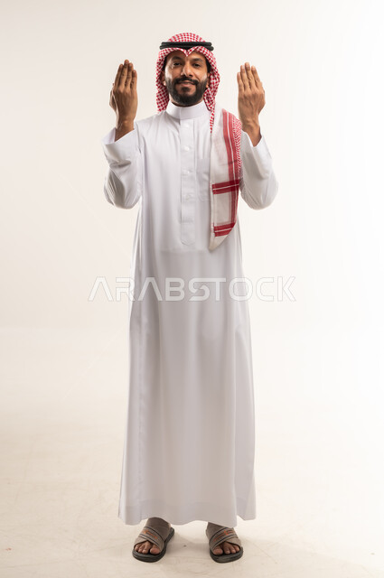 الإجتهاد في العبادة والحفاظ على الطاعات، بورتريه لرجل عربي خليجي بحريني يرتدي الثوب التقليدي والشماغ ينظر الى الكاميرا بتعابير الفرح والسرور، شاب سعودي يقوم بعرض ظاهر الكف، صورة الجسم بالطول الكامل، خلفية بيضاء
