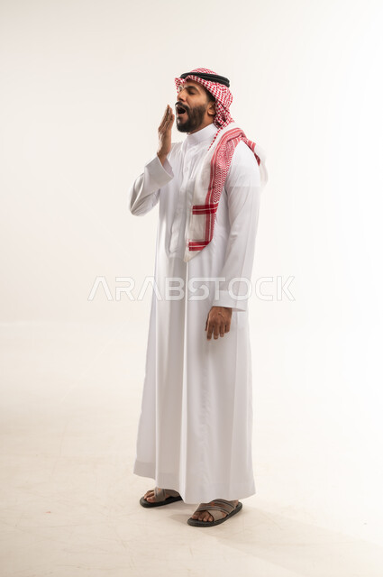 الشعور بالتعب والحاجة الى النوم والراحة, شاب سعودي يقف بتعابير الكسل والخمول و الإرهاق، بورتريه  لرجل عربي خليجي بحريني يرتدي الثوب التقليدي والشماغ يضع يده على فمه بإيماءات التثاؤب والنعاس، صورة الجسم بالطول الكامل, خلفية بيضاء
