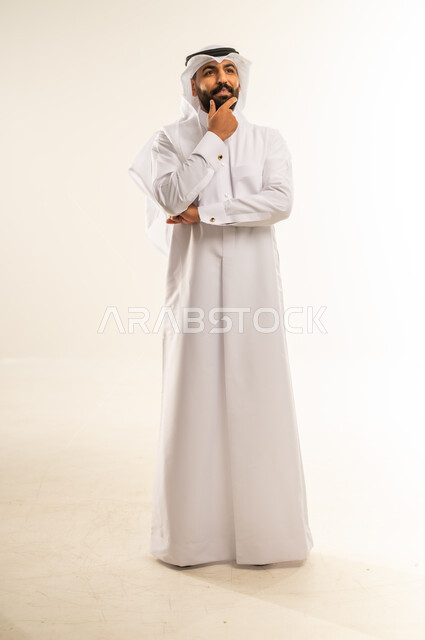التطلع والتخطيط للمستقبل، حل المشكلات واتخاذ القرارات، بورتريه لرجل عربي خليجي قطري يرتدي الغترة والثوب التقليدييضع يده على ذقنه بإيماءات التفكير وشرود الذهن، مفهوم الاستماع والتركيز، صورة الجسم بالطول الكامل، خلفية بيضاء