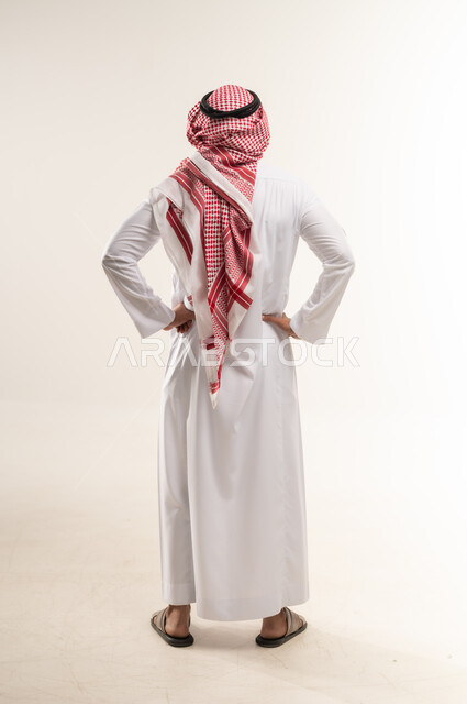 الحاجه للراحه من التعب والإرهاق , شاب سعودي يشعر بألم في العمود الفقري , بورتريه من الخلف  لرجل عربي خليجي بحريني يرتدي الثوب التقليدي والشماغ ينحني  ويضع يده اسفل ظهره بتعابير الشعور بالوجع, طلب المساعده للذهاب الى الطبيب ,صورة الجسم بالكامل، خلفية بيضاء