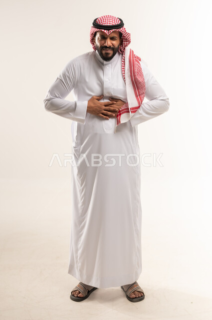 طلب المساعده للذهاب الى الطبيب، رجل سعودي يشعربعسر الهضم وحرقة في المعدة، بورتريه لشاب عربي خليجي بحريني يرتدي الثوب التقليدي والشماغ يمسك بطنه بتعابير الشعور بالألم، الإحساس بالمغص و التعب والإرهاق، الحاجة للدواء ووضع خطة علاجية، صورة الجسم بالكامل، خلفية بيضاء
