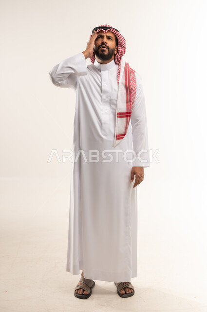 الحاجه للعلاج و طلب المساعده, الإحساس بالدوار والتعب والإرهاق, بورتريه لرجل عربي خليجي بحريني يرتدي الثوب التقليدي والشماغ يضع يده على رأٍسه بإيماءات الوجع, شاب سعودي يشعر بالصداع و ألم بالرأس, صورة الجسم بالطول الكامل، خلفية بيضاء