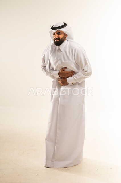 عسر الهضم والشعور بحرقة في المعدة، الحاجة للدواء ووضع خطة علاجية, الإحساس بالمغص و التعب والإرهاق, بورتريه لرجل عربي خليجي قطري يرتدي الثوب التقليدي والغترة يمسك بطنه بإيماءات الألم،  طلب المساعده للذهاب الى الطبيب، صورة الجسم بالطول الكامل، خلفية بيضاء