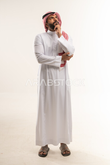 الشعور بالضيق والملل، التمعن والتركيز لإيجاد حل لمشكلة ما، المشكلات واتخاذ القرارات، بورتريه لشاب عربي خليجي بحريني يرتدي الثوب التقليدي والشماغ يضع يده خلف ذقنه، رجل سعودي ينظر الى الاعلى بإيماءات التفكير والحيرة، صورة الجسم بالطول الكامل, خلفية بيضاء