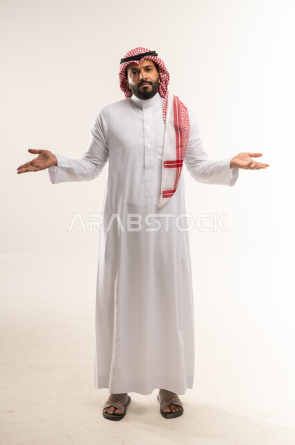 التردد وعدم الثقة بخصوص أمر معين، بورتريه لشاب عربي خليجي بحريني يرتدي الثوب التقليدي والشماغ يقف ويرفع كفيه للاعلى بإيماءات عدم التأكد، رجل سعودي ينظر الى الكاميرا بتعابير الحيرة وعدم المعرفة، صورة الجسم بالطول الكامل, خلفية بيضاء