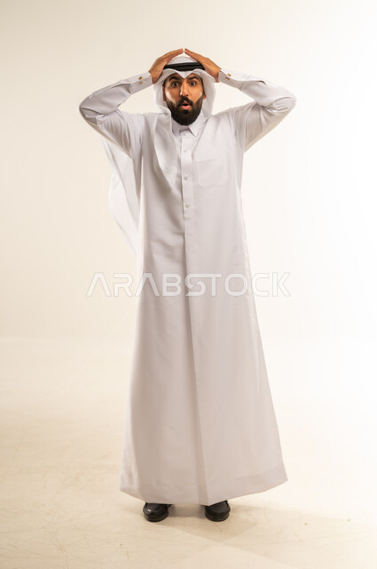 Shock and disbelief, gestures of surprise and amazement, concern with appearance, disappointment and negative feelings, portrait of a Qatari Gulf Arab man wearing traditional thobe and ghutra with his hands on his head, full body, white background
