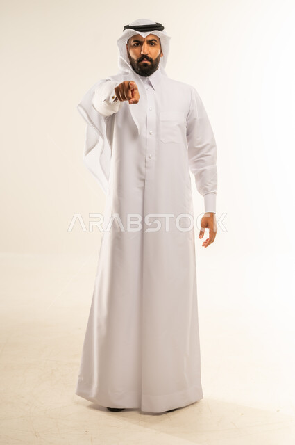 الإشارة باصبع السبابة إلى الكاميرا بشكل مباشر، التهديد والتوعد بتنفيذ شيء ما، إيماءات الترهيب والتحذير، توجيه أصابع الاتهام إلى شخص معين، بورتريه لرجل عربي خليجي قطري يرتدي الثوب التقليدي والغتره يشير إلى مكان ما محدد، الجسم بالطول الكامل، خلفية بيضاء