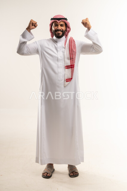 Looking at the camera with gestures of strength and pride, biceps movement, building an athletic body, maintaining physical fitness, portrait of a Bahraini Gulf Arab man wearing a traditional thobe and shemagh raising his hands up, full body length, white background