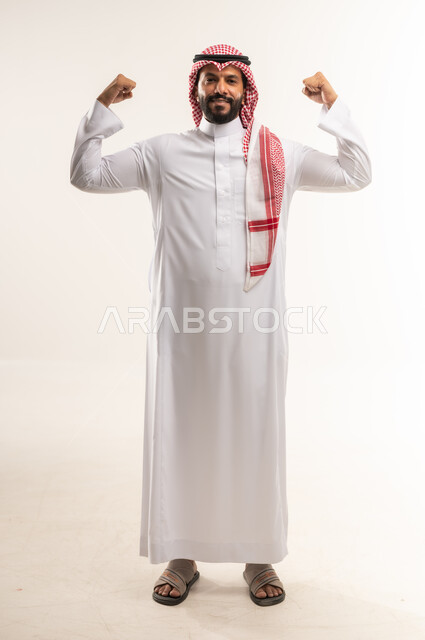 حركة العضلات ذات الرأسين, بناء جسم رياضي، المحافظة على اللياقه البدنيه، بورتريه لرجل عربي خليجي بحريني يرتدي الثوب التقليدي والشماغ يرفع يديه نحو الأعلى, النظر إلى الكاميرا بايماءات القوة والافتخار, الطول الكامل للجسم، خلفية بيضاء