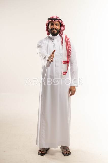 التعارف و الصداقه وتكوين علاقات, بورتريه لرجل عربي خليجي بحريني مبتسم يرتدي الثوب التقليدي والشماغ  يقوم بمد كفه للمصافحة بإيماءات السرور، النظر الى الكاميرا بتعابير البشاشة،  إلقاء التحيه والسلام, مفهوم الاستقبال والترحيب, الطول الكامل للجسم، خلفية بيضاء