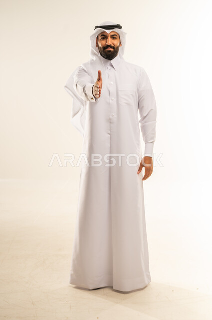 مد كف يد نحو الأمام للمصافحة، إلقاء التحية والسلام، الأناقة والوسامة والرجولة، مفهوم التقدير والاحترام، بورتريه لرجل عربي خليجي قطري مبتسم يرتدي الثوب التقليدي والغتره ينظر إلى الكاميرا بإيماءات السعادة والسرور، الجسم بالطول الكامل، خلفية بيضاء