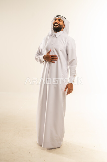 Joy, happiness and having a good time, closing eyes and laughing hard, hearing some funny news, joking and telling jokes, portrait of a smiling Qatari Gulf Arab man wearing traditional thobe and ghutra holding his stomach and laughing, full body, white background