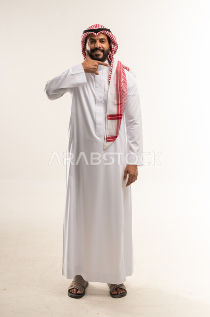 انتظار مكالمة وإستخدام الميكروفون، بورتريه لرجل عربي خليجي بحريني مبتسم يرتدي الثوب  التقليدي والشماغ يرفع يده بإيماءات الإتصال، إجراء مكالمة هاتفية بايماءات البشاشة، تعابير الفرح والسرور، الطول الكامل للجسم, خلفية بيضاء