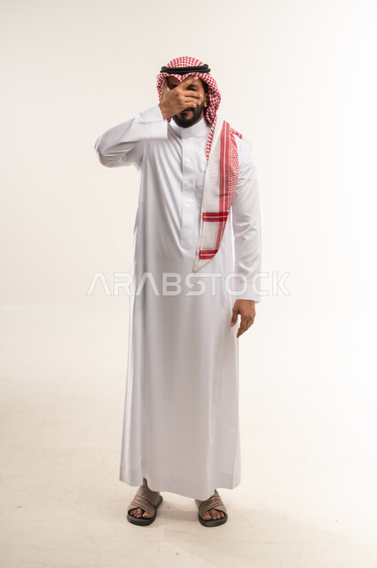 Expressions of shyness and modesty, remembering something suddenly, portrait of a Bahraini Gulf Arab man wearing traditional thobe and shemagh covering his eyes with his hand with gestures of happiness, feeling joy and pleasure, full body length, white background