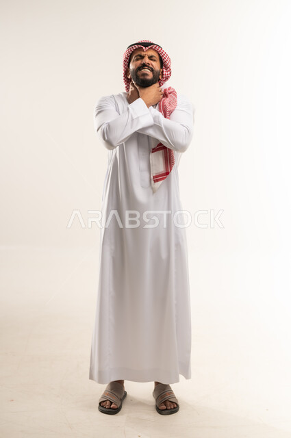 الاحساس بألم البلعوم, الحاجة إلى العلاج والدواء, مفهوم الاهتمام بالصحة, الاصابة بنزلة برد والتهاب الحلق، بورتريه لرجل عربي خليجي بحرين يرتدي الثوب التقليدي والشماغ يضع يديه على حلقه ويشعر بالاختناق, الطول الكامل للجسم، خلفية بيضاء