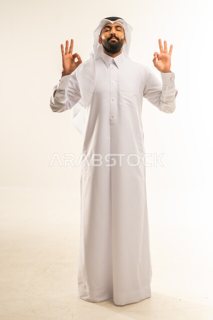 الشعور بالرضا والاستحسان، التعبير عن الإعجاب والتقدير، رفع اليدين بعلامات الجودة والقبول، الامتياز والعلامة الكاملة، بورتريه لرجل عربي خليجي قطري مبتسم يرتدي الثوب التقليدي والغتره ينظر إلى الكاميرا بإيماءات السعادة والسرور، الجسم بالطول الكامل، خلفية بيضاء
