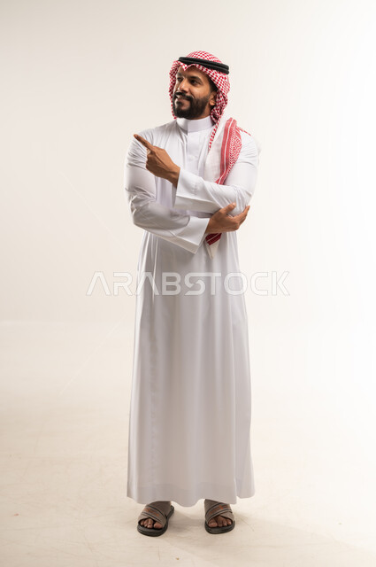 Pointing and explaining something, specifying a specific location, indicating the location of an item, portrait of a Bahraini Gulf Arab man wearing a traditional thobe and shemagh pointing with his index finger to a specific target, gestures of happiness and pleasure, full body length, white background