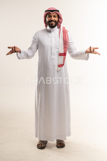 Standing with gestures of surprise and astonishment, feeling happy and pleased to hear the expected news, portrait of a Bahraini Gulf Arab man wearing traditional thobe and shemagh raising his hands with expressions of shock, astonishment and amazement, surprised and astonished by something, full body length, white background