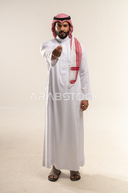مفهوم الصبر والتريث و التأني, التهديد و التوعد لشيء ما بتعابير الغضب، بورتريه لرجل عربي خليجي بحريني يرتدي الثوب التقليدي والشماغ ينظر الى الكاميرا يرفع يده نحو الأعلى بإيماءات طلب الإنتظار, إمهال بعض الوقت لفعل شيء، الطول الكامل للجسم, خلفية بيضاء