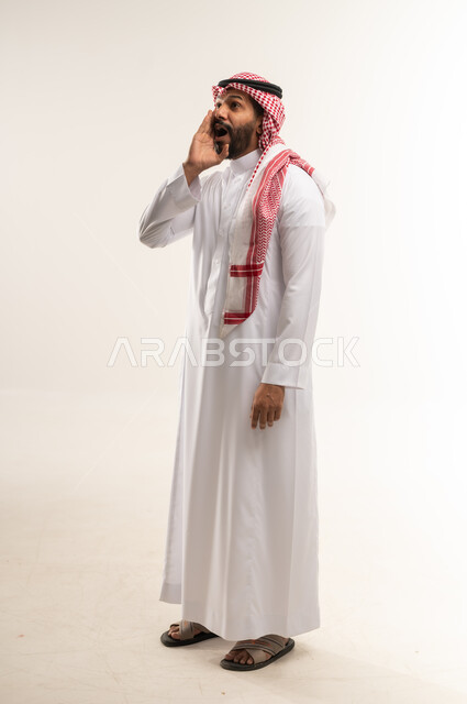 النداء والكلام والتحدث بصوت مرتفع، بورتريه لرجل عربي خليجي بحريني يرتدي الثوب التقليدي والشماغ يضع يده على فمه بإيماءات المناداة لشخص ما، دردشة ومحادثات وتواصل اجتماعي، الطول الكامل للجسم, خلفية بيضاء
