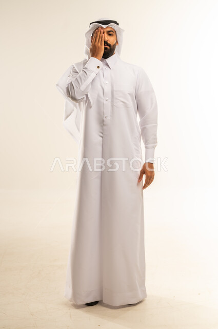 وضع اليد على العين وتغطيها، التهاب واحمرار العيون والحاجة لزيارة الطبيب، ضعف النظر وتشوش الرؤية، التعرض لأذية في الشبكية، بورتريه لرجل عربي خليجي قطري يرتدي الثوب التقليدي والغترة يعاني من مشاكل صحية في عينه، الجسم بالطول الكامل، خلفية بيضاء