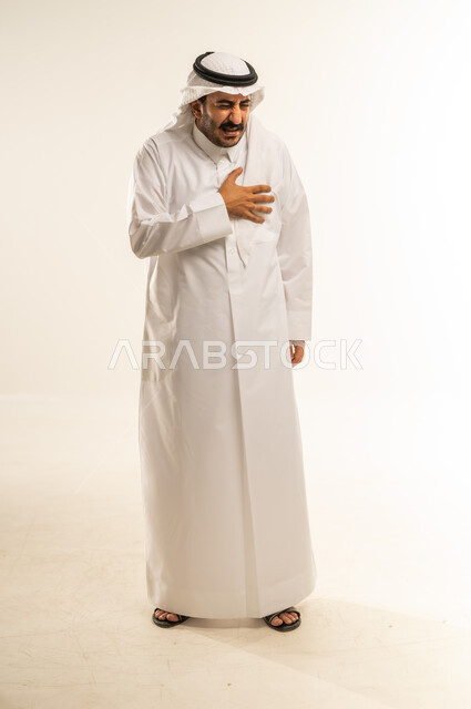 الإحساس بوخزات في الصدر، مشاكل صحية في الرئتين والجهاز التنفسي، التعرض لذبحة صدرية، أمراض القلب المزمنة والأوعية الدموية، بورتريه لرجل عربي خليجي قطري يرتدي الثوب التقليدي والغترة يضع يده على قلبه بإيماءات التألم الشديد، الجسم بالطول الكامل، خلفية بيضاء