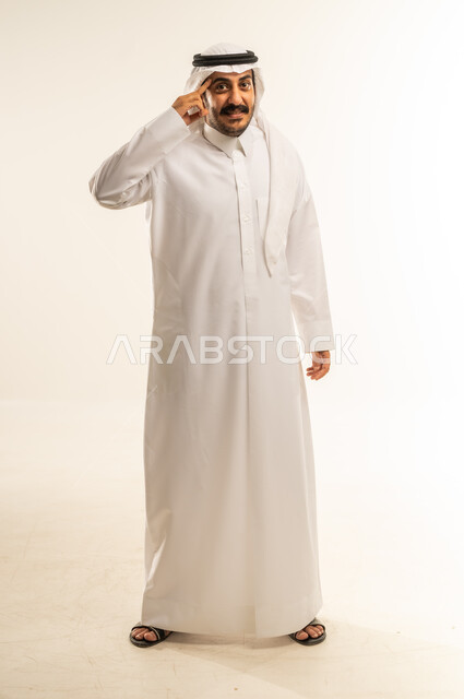 الإشارة إلى الرأس بإيماءات الثقة بالنفس، مفهوم الحكمة و الوعي، التفكير بشكل صحيح وسليم، المقدرة على حل المشكلات وإعطاء النصائح، بورتريه لرجل عربي خليجي قطري مبتسم يرتدي الثوب التقليدي والغتره ينظر إلى الكاميرا بتعابير البشاشة، الجسم بالطول الكامل، خلفية بيضاء