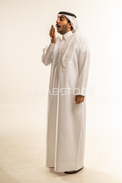 الشعور بالنعاس والحاجة للنوم، ضرورة أخذ قسط من الراحة والاسترخاء، إيماءات التعب والإرهاق، بورتريه لرجل عربي خليجي قطري مبتسم يرتدي الثوب التقليدي والغتره يقوم بوضع يضع يده أمام فمه والتثاؤب، الجسم بالطول الكامل، خلفية بيضاء