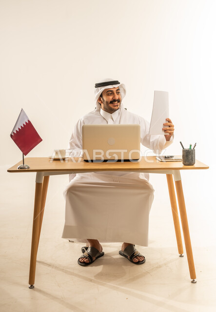 Utilizing modern technologies in administrative and office work, auditing papers and files, employment in Qatari offices and companies, portrait of a Qatari Gulf Arab man wearing traditional thobe and ghutra sitting behind a desk with the Qatari flag next to him and a laptop in front of him, white background