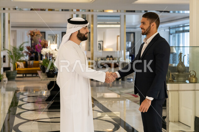 المصافحة وبناء العلاقات الاجتماعية الناجحة, مشاركة الأصدقاء الأوقات الممتعة, التعارف وتكوين الصداقات, الاستمتاع بالجلسات الشبابية في المطعم, رجل عربي خليجي إماراتي يرتدي الكندورة والغترة البيضاء يصافح صديقه في إحدى المطاعم بالإمارات