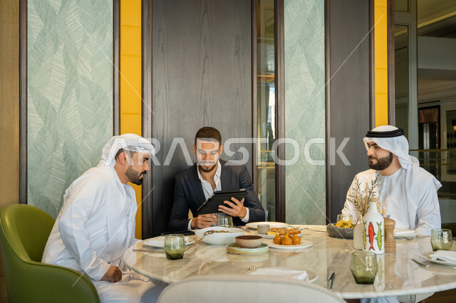 الحوارات والنقاشات بين الزملاء, استخدام الأجهزة التقنية الحديثة, مجموعة من الأصدقاء العربيين الخليجيين الإماراتيين يجلسون على المائدة في إحدى المطاعم بالإمارات ويقومون باستعمال الجهاز اللوحي, قضاء الأوقات الممتعة في المطعم