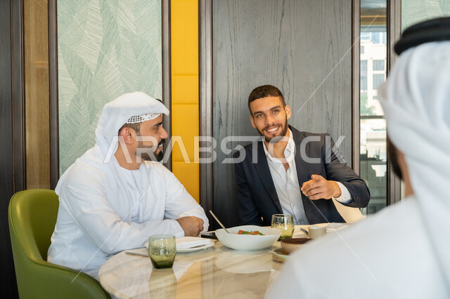 الاستمتاع بتناول الغداء في المطعم, مشاركة الأصدقاء الأوقات الممتعة, تبادل الأحاديث والاخبار, بناء علاقات اجتماعية ناجحة, مجموعة من الأصدقاء العربيين الخليجيين الإماراتيين يجلسون على المائدة في إحدى المطاعم في الإمارات بإيماءات السعادة والسرور