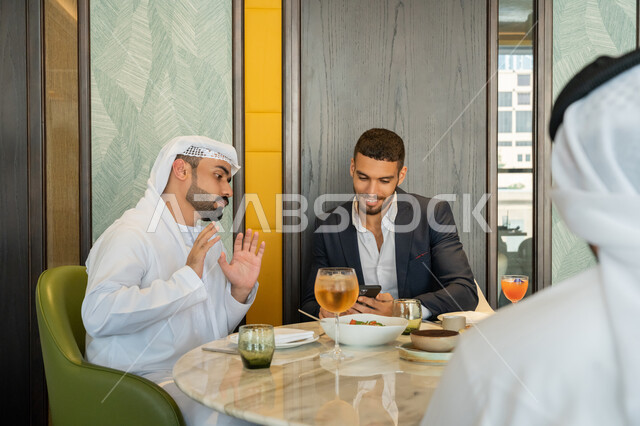 استخدام الأجهزة التقنية الحديثة, الحوارات والنقاشات بين الزملاء, مجموعة من الأصدقاء العربيين الخليجيين الإماراتيين يجلسون على المائدة في إحدى المطاعم بالإمارات ويقومون باستعمال الجهاز اللوحي, قضاء الأوقات الممتعة في المطعم