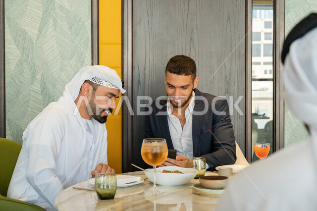 الحوارات والنقاشات بين الزملاء, استخدام الأجهزة التقنية الحديثة, مجموعة من الأصدقاء العربيين الخليجيين الإماراتيين يجلسون على المائدة في إحدى المطاعم بالإمارات ويقومون باستعمال الجهاز اللوحي, قضاء الأوقات الممتعة في المطعم