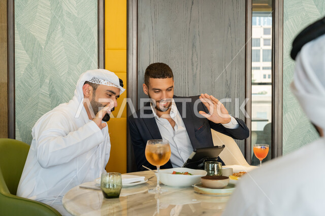 Having fun in a restaurant, using modern technology, conversations and discussions between colleagues, a group of Emirati Gulf Arab friends sitting at a table in a restaurant in the Emirates and making a video call via a tablet