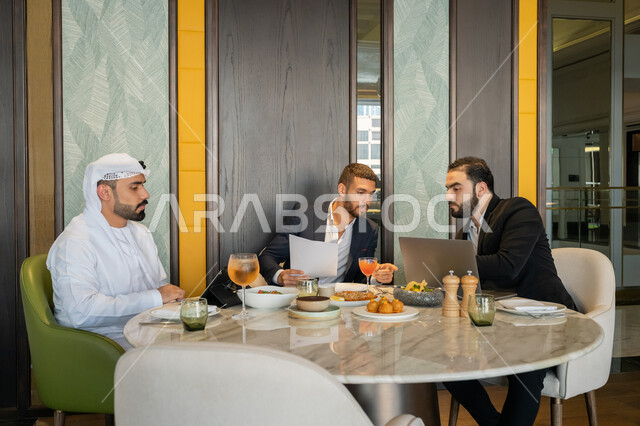 استخدام الأجهزة التقنية الحديثة, الحوارات والنقاشات بين الزملاء, استعمال جهاز الحاسوب المحمول, مناقشة مهام العمل في المطعم, مجموعة من الأصدقاء العربيين الخليجيين السعوديين يجلسون على المائدة في إحدى المطاعم في الإمارات