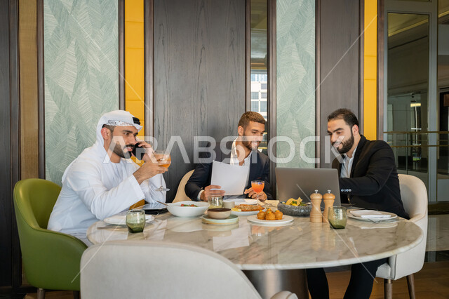 مناقشة مهام العمل في المطعم, استخدام الأجهزة التقنية الحديثة, الحوارات والنقاشات بين الزملاء, استعمال جهاز الحاسوب المحمول, مجموعة من الأصدقاء العربيين الخليجيين السعوديين يجلسون على المائدة في إحدى المطاعم في الإمارات