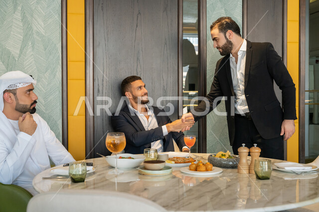 المصافحة وبناء العلاقات الاجتماعية الناجحة, مشاركة الأصدقاء الأوقات الممتعة, تبادل الأحاديث والاخبار, الاستمتاع بتناول الغداء في المطعم, مجموعة من الأصدقاء العربيين الخليجيين الإماراتيين يجلسون على المائدة في إحدى المطاعم في الإمارات بإيماءات السعادة والسرور