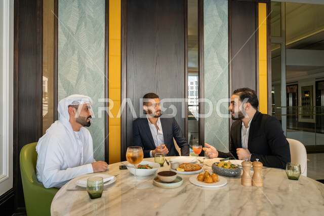 الاستمتاع بتناول الغداء في المطعم, مشاركة الأصدقاء الأوقات الممتعة, تبادل الأحاديث والاخبار, بناء علاقات اجتماعية ناجحة, مجموعة من الأصدقاء العربيين الخليجيين الإماراتيين يجلسون على المائدة في إحدى المطاعم في الإمارات بإيماءات السعادة والسرور