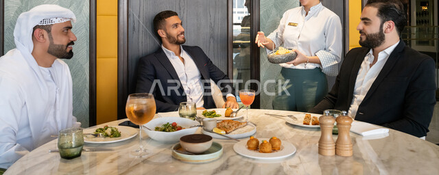 تبادل الأحاديث والاخبار, مشاركة الأصدقاء الأوقات الممتعة, الاستمتاع بتناول الغداء في المطعم, بناء علاقات اجتماعية ناجحة, صورة مقربة لمجموعة من الأصدقاء العربيين الخليجيين الإماراتيين يجلسون على المائدة في إحدى المطاعم في الإمارات ويقومون بتناول الطعام