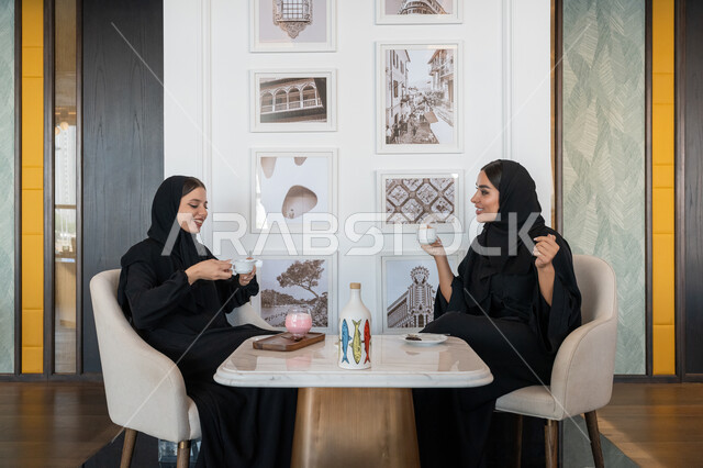 قضاء أوقات ممتعة ومسلية مع الأصدقاء, بناء علاقات اجتماعية ناجحة, النقاشات والحوارات في الأجواء الهادئة، امرأة عربية خليجية إماراتية محجبة ترتدي العباءة السوداء تجلس مع صديقتها بإحدى المقاهي, شابتان سعوديتان تستمتعان بالمشروبات الباردة