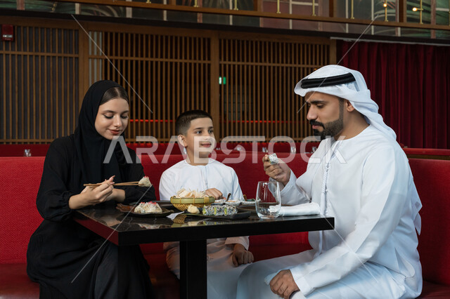 مطاعم وكافيهات الإمارات, قضاء الأوقات الممتعة في المطعم, مشاركة الأحاديث والأخبار مع العائلة, الأجواء العائلية السعيدة, عائلة عربية خليجية إماراتية يرتدون الثوب الإماراتي التقليدي يجلسون على المائدة ويقومون بتناول الطعام