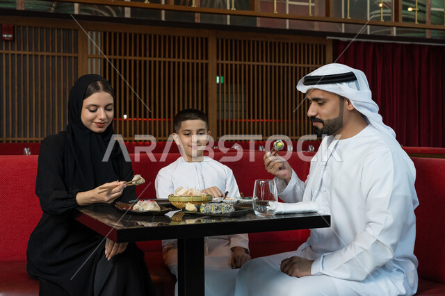 مطاعم وكافيهات الإمارات, قضاء الأوقات الممتعة في المطعم, مشاركة الأحاديث والأخبار مع العائلة, الأجواء العائلية السعيدة, عائلة عربية خليجية إماراتية يرتدون الثوب الإماراتي التقليدي يجلسون على المائدة ويقومون بتناول الطعام