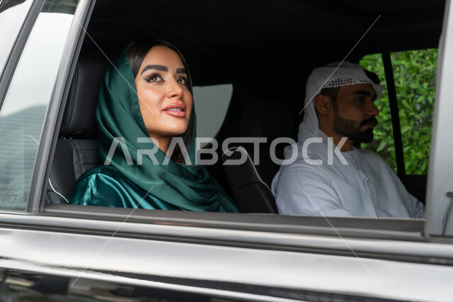 استخدام التاكسي للوصول إلى الوجهة المطلوبة, خدمة توصيل الركاب, خدمات النقل الآمنة في الإمارات العربية المتحدة، صورة مقربة لامرأة عربية خليجية إماراتية ترتدي العباءة الملونة تجلس داخل السيارة مع زوجها وتنظر بإيماءات السعادة والسرور