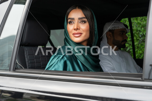 خدمة توصيل الركاب، استخدام التاكسي للوصول إلى الوجهة المطلوبة, خدمات النقل الآمنة في الإمارات العربية المتحدة، صورة مقربة لامرأة عربية خليجية إماراتية ترتدي العباءة الملونة تجلس داخل السيارة مع زوجها وتنظر بإيماءات السعادة والسرور
